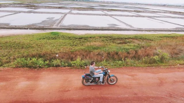 Drone view following a motorcycle rider on a dirt road trail adventure in Asia; camera list higher to bird's eye perspective