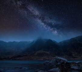 Composite image of Winter landscape of snowcapped Mountain Range at night with Milky Way above