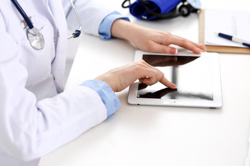 Doctor working table. Woman physician using tablet computer while sitting in hospital office close-up. Healthcare, insurance and medicine concept