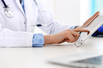 Fototapeta premium Doctor working table. Woman physician using tablet computer while sitting in hospital office close-up. Healthcare, insurance and medicine concept