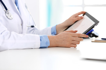 Doctor working table. Woman physician using tablet computer while sitting in hospital office close-up. Healthcare, insurance and medicine concept