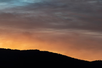 Fototapeta na wymiar Orange cloudy sunset with mountain silhouette