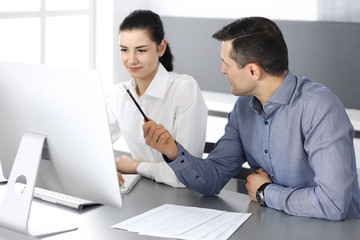 Fototapeta premium Cheerful smiling businessman and woman working with computer in modern office. Headshot at meeting or workplace. Teamwork, partnership and business concept 
