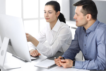 Cheerful smiling businessman and woman working with computer in modern office. Headshot at meeting or workplace. Teamwork, partnership and business concept 