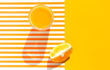 Glass of freshly squeezed orange juice with pulp fruit wedge on duotone bright sunny yellow and white striped background. Harsh light hard shadows. Summer vacation beach tropical concept