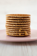 Stack of homemade Dutch stroopwafels with honey-caramel filling on pink plate, side view. Closeup.