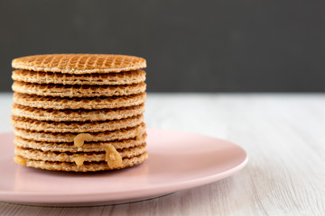 Stack of sweet Dutch stroopwafels with honey-caramel filling on pink plate, side view. Copy space.
