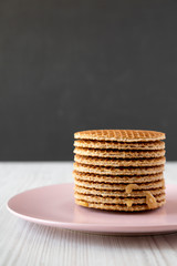 Stack of homemade Dutch stroopwafels with honey-caramel filling on pink plate, side view. Close-up.