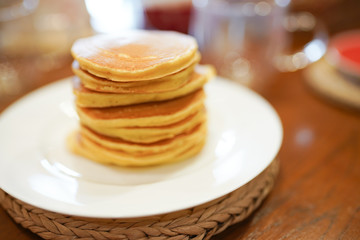 High stack of pancakes on white plate on wooden table in the kitchen . Breakfast or dinner for the whole family