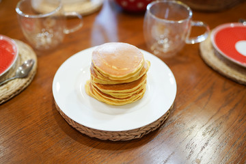 High stack of pancakes on white plate on wooden table in the kitchen . Breakfast or dinner for the whole family