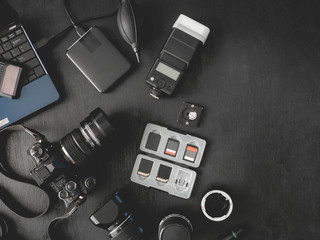 top view of work space photographer with digital camera, flash, cleaning kit, memory card, external harddisk, USB card reader, laptop and camera accessory on black table background