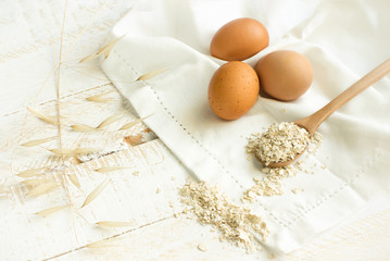 Free range organic brown eggs spilled oats on wooden spoon on white cotton towel wooden table. Balanced diet baking cooking ingredients concept. Skin care home remedies