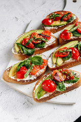 Homemade sandwiches with cream cheese. tomatoes, avocado, spinach and arugula on a white board