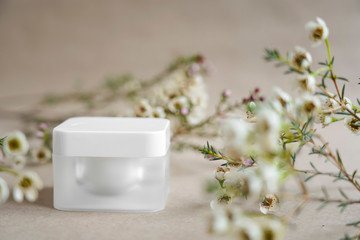 White square cosmetic jar on a beige background decorated with white flowers