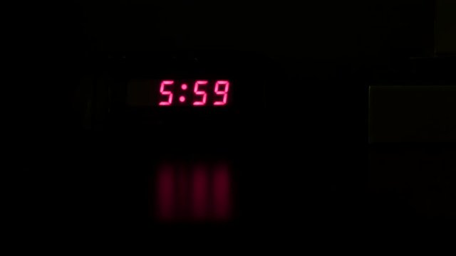 alarm goes off in dark room and man pulls clock out of shot