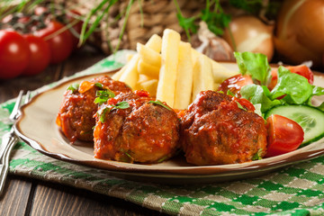 Roasted meatballs in tomato sauce with french fries and salad