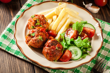 Roasted meatballs in tomato sauce with french fries and salad