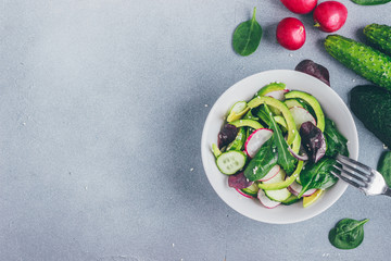 Healthy salad with radishes, avacado, cucumbers, spinach and arugula in a bowl top view