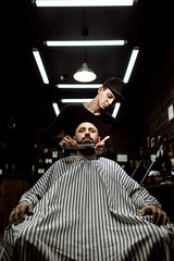 Obraz na płótnie Canvas The stylish barbershop. The fashion barber tidies up beard of brutal man sitting in the armchair