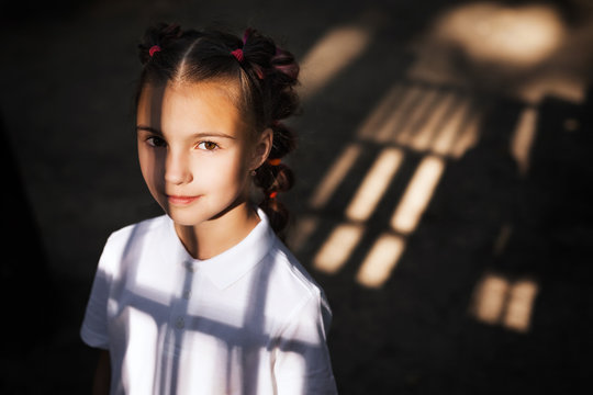 cute little thoughtful girl standing at the night playground. shadows from gungle gym falling on her face and body