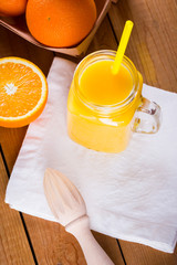 Orange fruits and juice on white napkin. Citrus fruit for making juice with manual juicer. Oranges in wooden box on wooden boards. Mason jar with orange juice