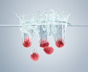 Lychee berries fall into the water scattering a lot of splashes and drops