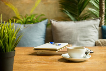 Cup of coffee with books and pen on wooden table in coffee shop.