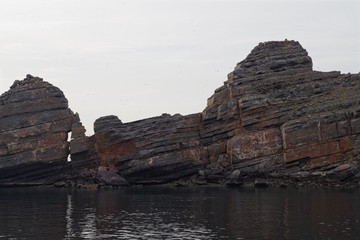 Layers of rocks emerging from the water. Geological background.