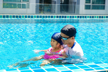 Cute little asian girl learning to swim with coach in swimming pool