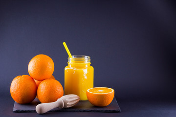 Orange fruits and juice on black background. Citrus fruit for making juice with manual juicer. Oranges on slate board. Mason jar with orange juice. Copy space