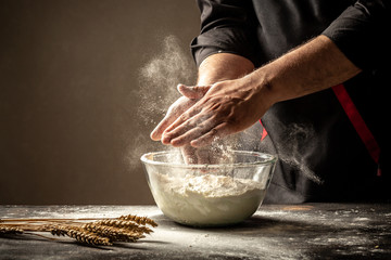 male hands making dough for pizza. White flour flying into air as pastry chef. Food concept