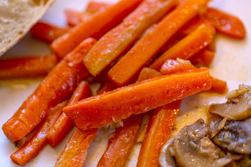 Fried carrots with mushrooms and garlic. Large juicy slices of sauteed vegetables on a plate. Cooked sliced carrots and mushrooms. Vegetarian food. Soft focus. Top view.