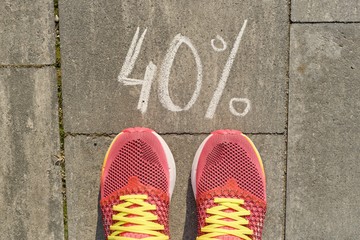 Text 40% written on gray pavement with woman legs in sneakers, view from above