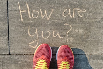 How are you? written on gray sidewalk with womens legs in sneakers, top view