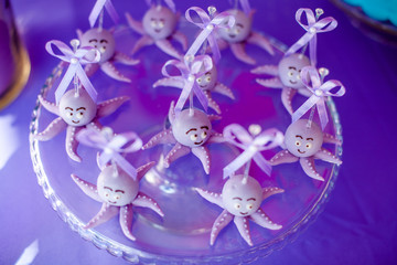 Purple cake pops funny octopuses shared on the glass round plate and jars whith marshmallow on purple background. Summer candy bar on the party, birthday