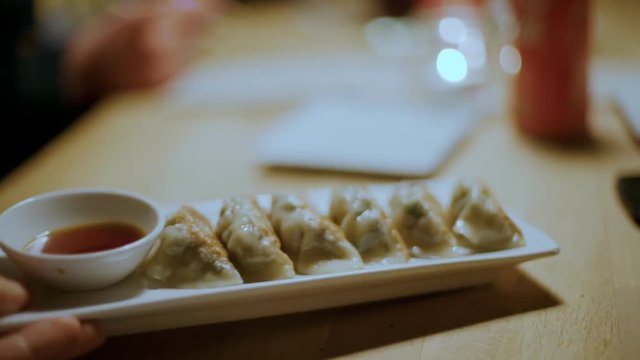 Group of friends in restaurant or cafe have funa dn enjoy delicious exotic food at tapas bar, asian dumplings or gyozas. Sharing food between people. Eat with chopsticks