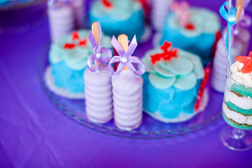 Birthday party concept. Table for kids with cupcakes with blue and red top and decored items in bright blue and purple colors. Summer season delicious on the party. Sea time theme on the candy bar