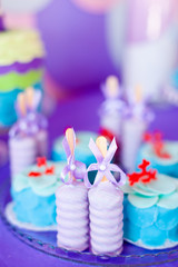 Birthday party concept. Table for kids with cupcakes with blue and red top and decored items in bright blue and purple colors. Summer season delicious on the party. Sea time theme on the candy bar