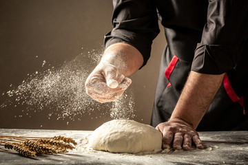 Man sprinkling flour over fresh dough on kitchen table. Food concept