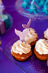 Birthday party concept for girl. Table for kids with cupcakes with withe topind decored purple mermaid tail. Summer season delicious on the party. Sea time theme on the candy bar