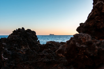 A small island near the shore being framed by the rocky beach