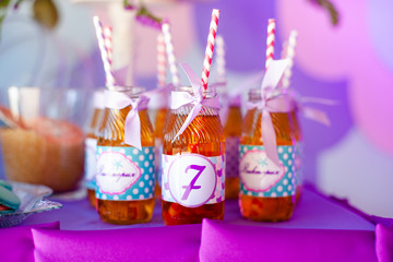Birthday party concept, candy bar for children. A lot of bottles of apple juice, special labels on it, white and pink straws on purple background