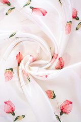 Silk wrinkled white fabric with pink flowers. View from above. Textile and texture concept - close up of crumpled silk white wavy fabric background