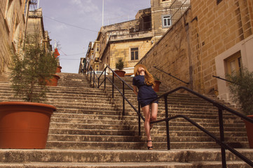 Fototapeta na wymiar Girl sitting on the railings of the stairs on the street, old city of the Three Cities