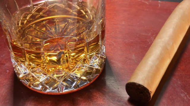 Close up of whiskey in glass and cigar sitting on mahogany bar top.
Starts in shadow and reveals into the light.