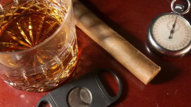 Whiskey glass, cigar, cigar cutter and old pocket watch sit on mahogany bar top.
Reveals out of shadows and then returns back into shadows.