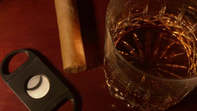 Whiskey glass, cigar and cigar cutter sit on mahogany bar top.
Reveals out of shadows and then returns back into shadows.
