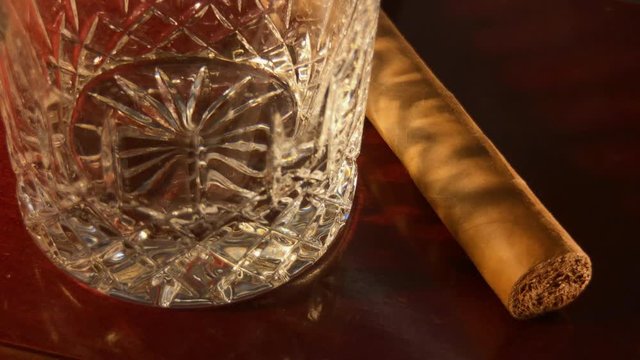 Close up of empty crystal glass and cigar coming out of shadow.
Whiskey is poured into glass.
