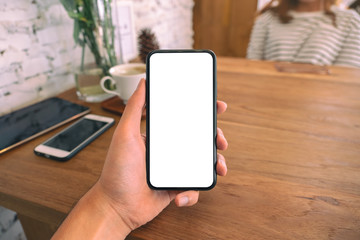 Mockup image of a man's hand holding black mobile phone with blank white screen with woman sitting in cafe