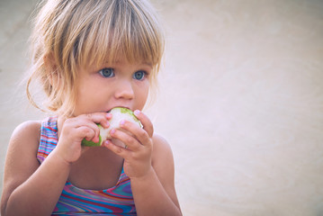 Cute adorable toddler girl eating fresh pear sitting on the beach.